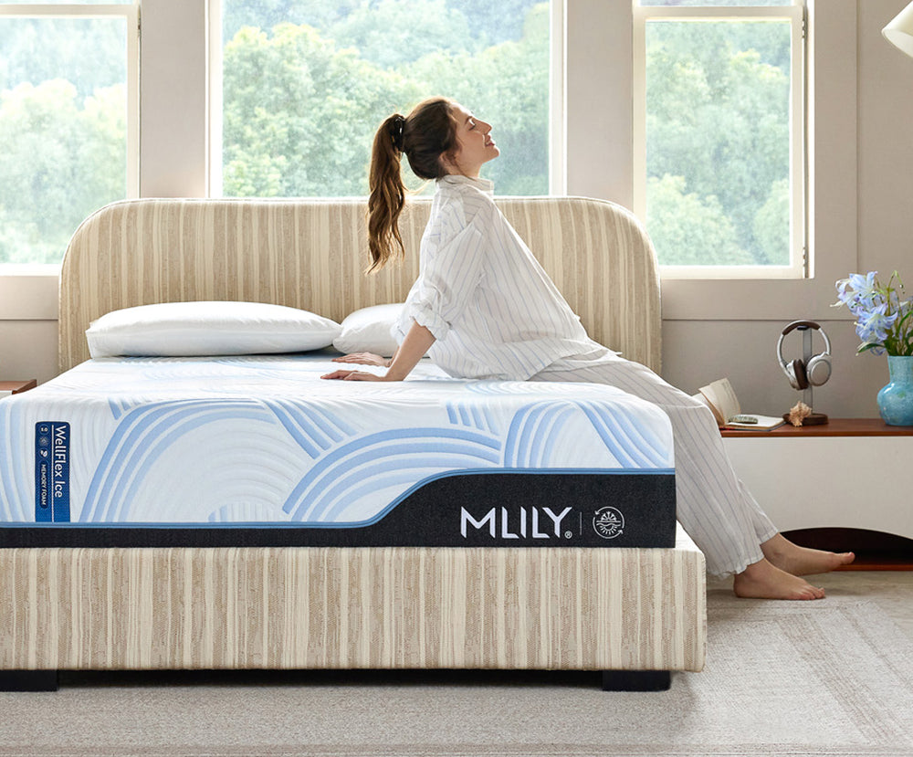 Woman sitting on a MLILY mattress in a bright room with large windows.