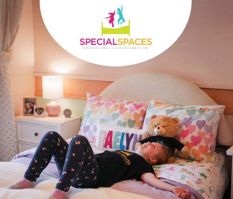 Child lying on a bed with colorful pillows and a teddy bear, in a room with 'Special Spaces' branding.