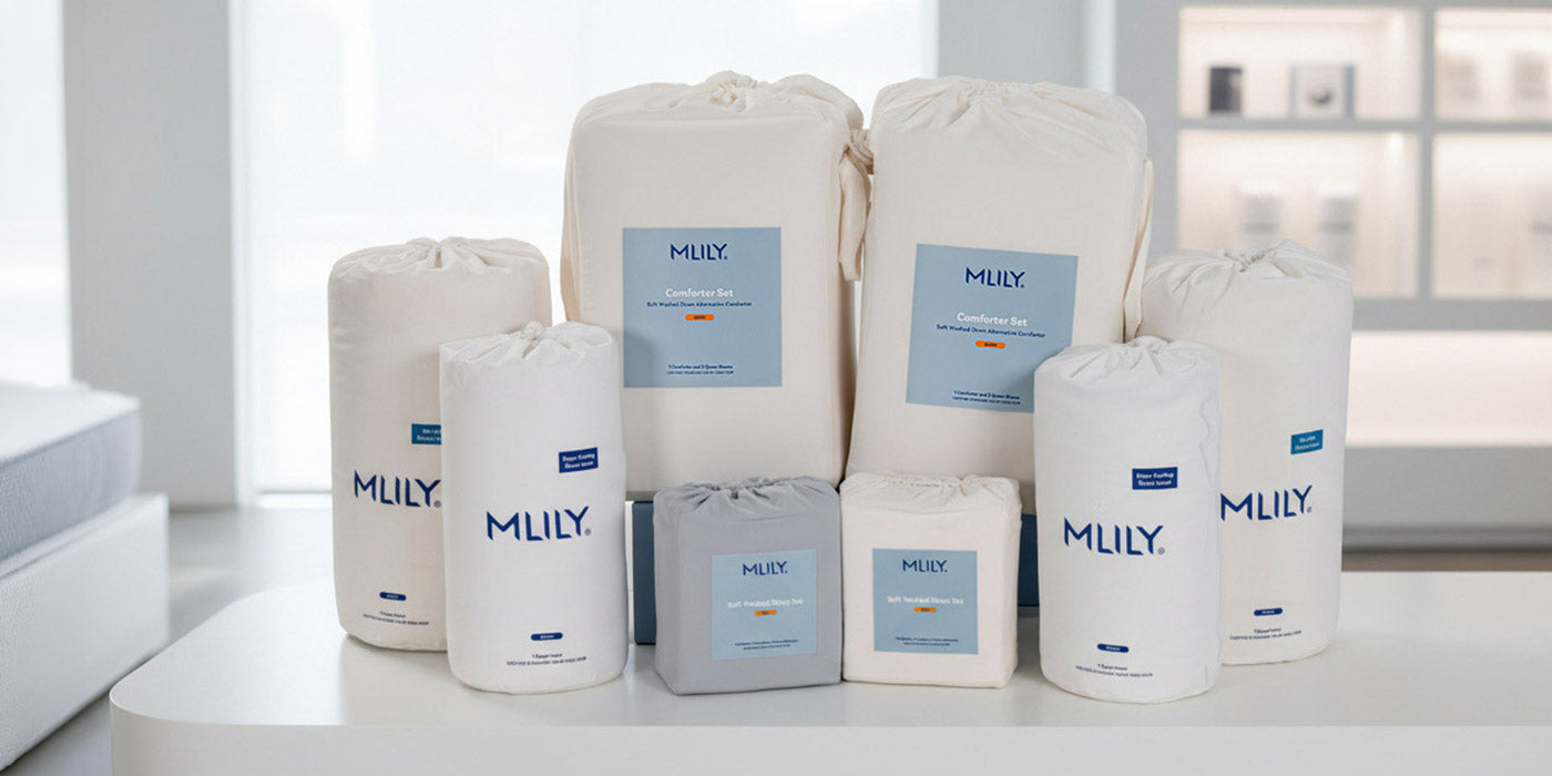 A collection of MLILY bedding storage bags and containers in white and light gray, arranged on a white table in a bright, modern bedroom setting.