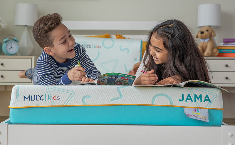 Children reading books on a MLILY Kids mattress with JAMA branding in a bedroom setting.