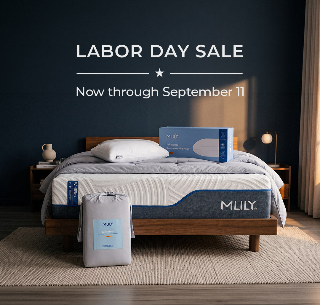 A bed with an MLILY mattress and bedding in a styled bedroom, with a matching mattress bag on the floor and an MLILY box on the bed. Large text at the top reads 'LABOR DAY SALE Now through September 11'.