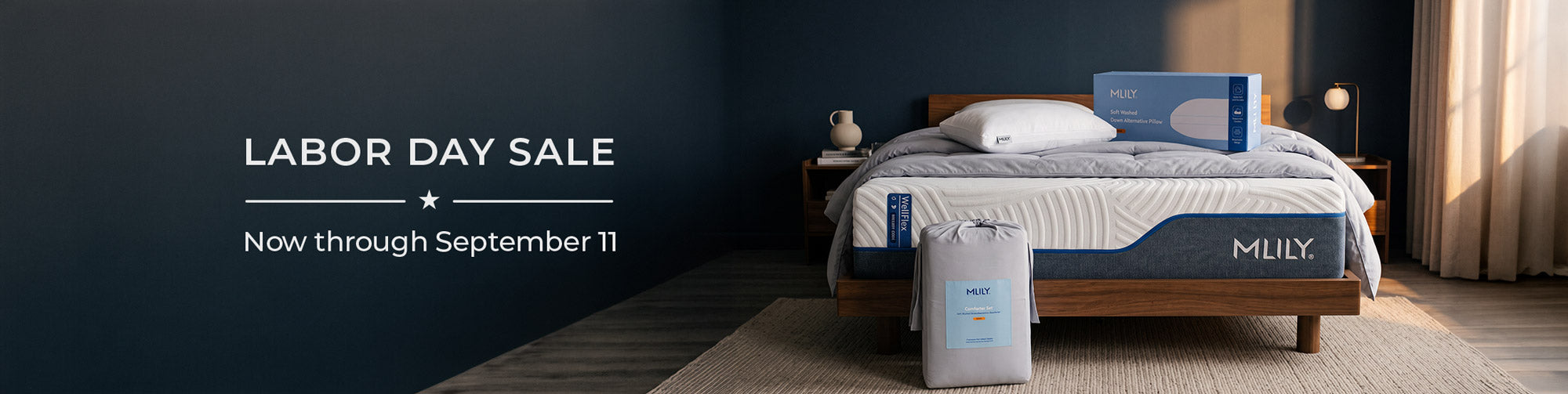 A bed with a white and blue mattress shown in a styled bedroom scene with dark blue walls, a wooden bed frame, and a pillow box labeled MLILY. Large sale text on the left reads 'LABOR DAY SALE Now through September 11'.