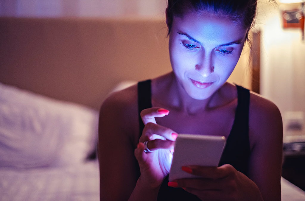 a smiling woman browses her smartphone as the phone emanates a bright glow on her face