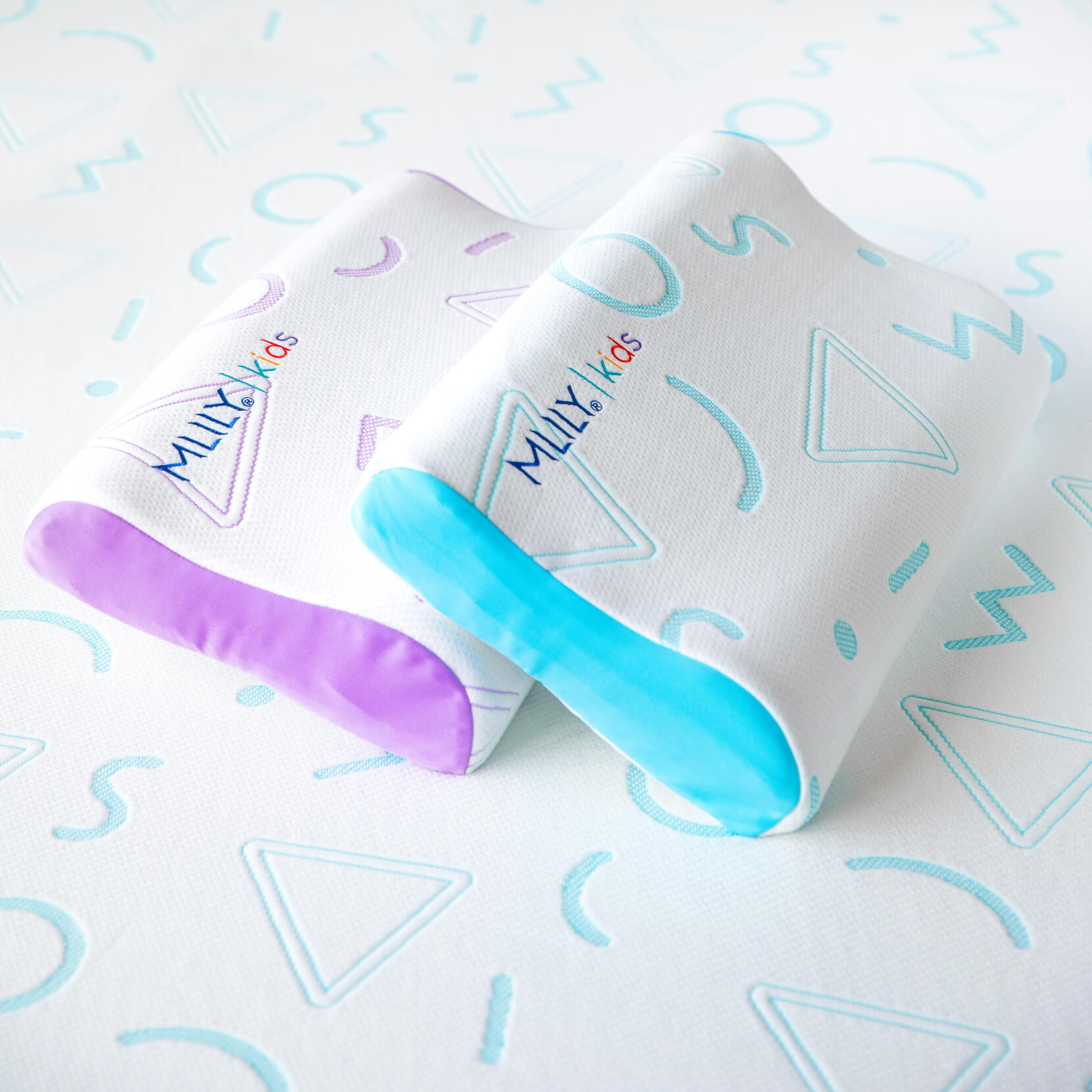 A stacked pair of white Jama pillows made of contoured memory foam, one features purple accents, and the other has teal accents.