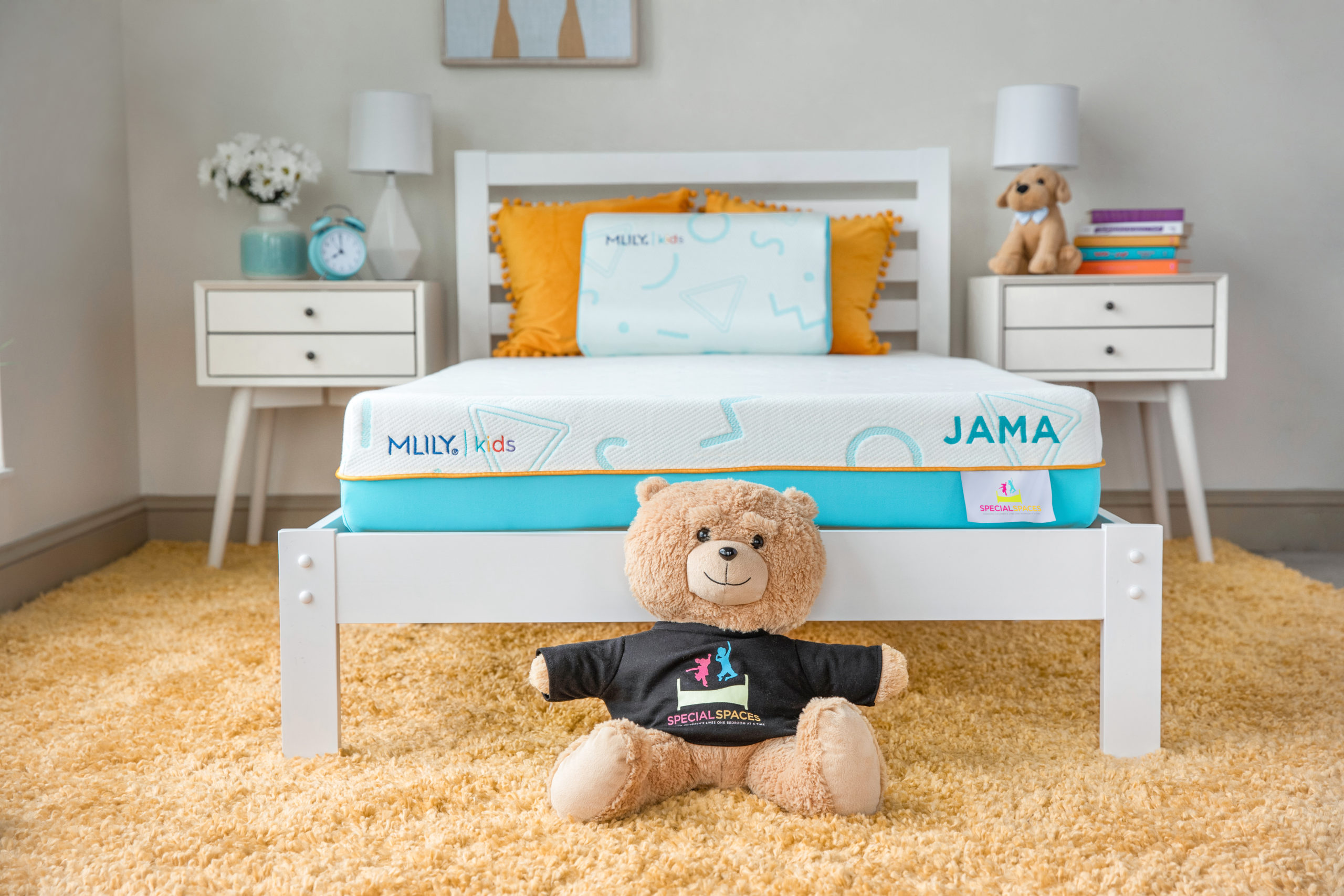 Stuffed bear sitting at foot of MLILY JAMA kids mattress on white bedframe between two bedside tables in kids bedroom .