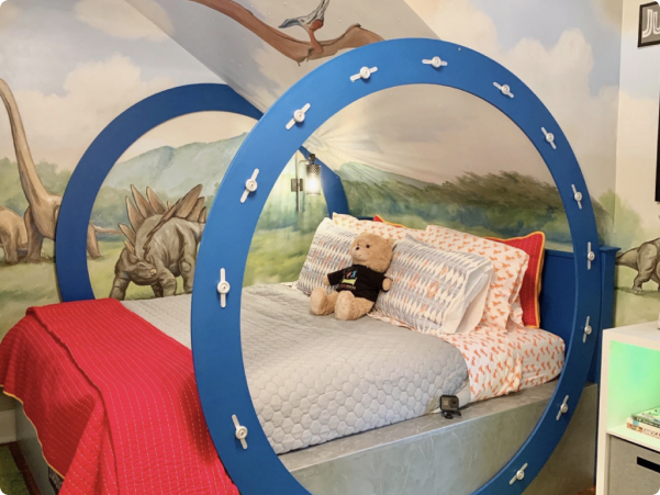 Child's bedroom with dinosaurs and landscape mural on walls and bed with large blue circles attached.