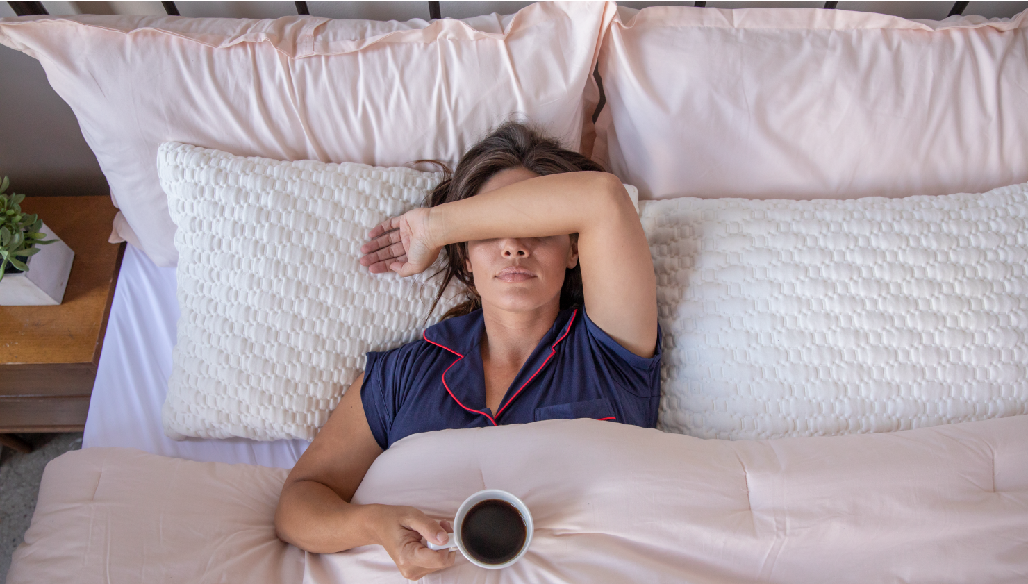 Woman laying sleeplessly in bed with a cup of coffee
